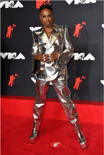 Billy porter standing on the red carpet with his high heels and silver outfit.